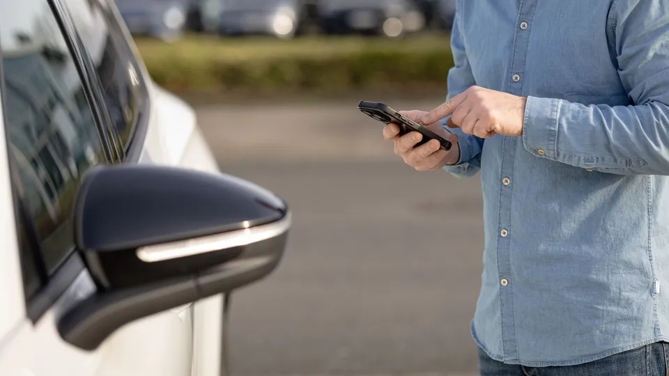 A man with a smartphone next to a white car