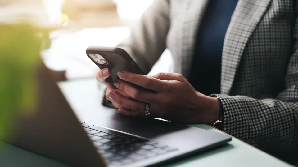 A person using a phone at a laptop