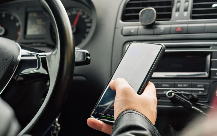 A driver holding a smartphone at the dashboard of a car