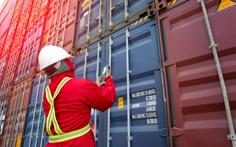 A worker in a hard hat checking shipping containers in a yard
